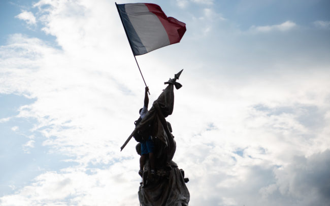 A homme est monté sur une statue avec un drapeau français.