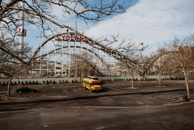A yellow bus is parked in front of the Cyclone attraction at Coney Island.